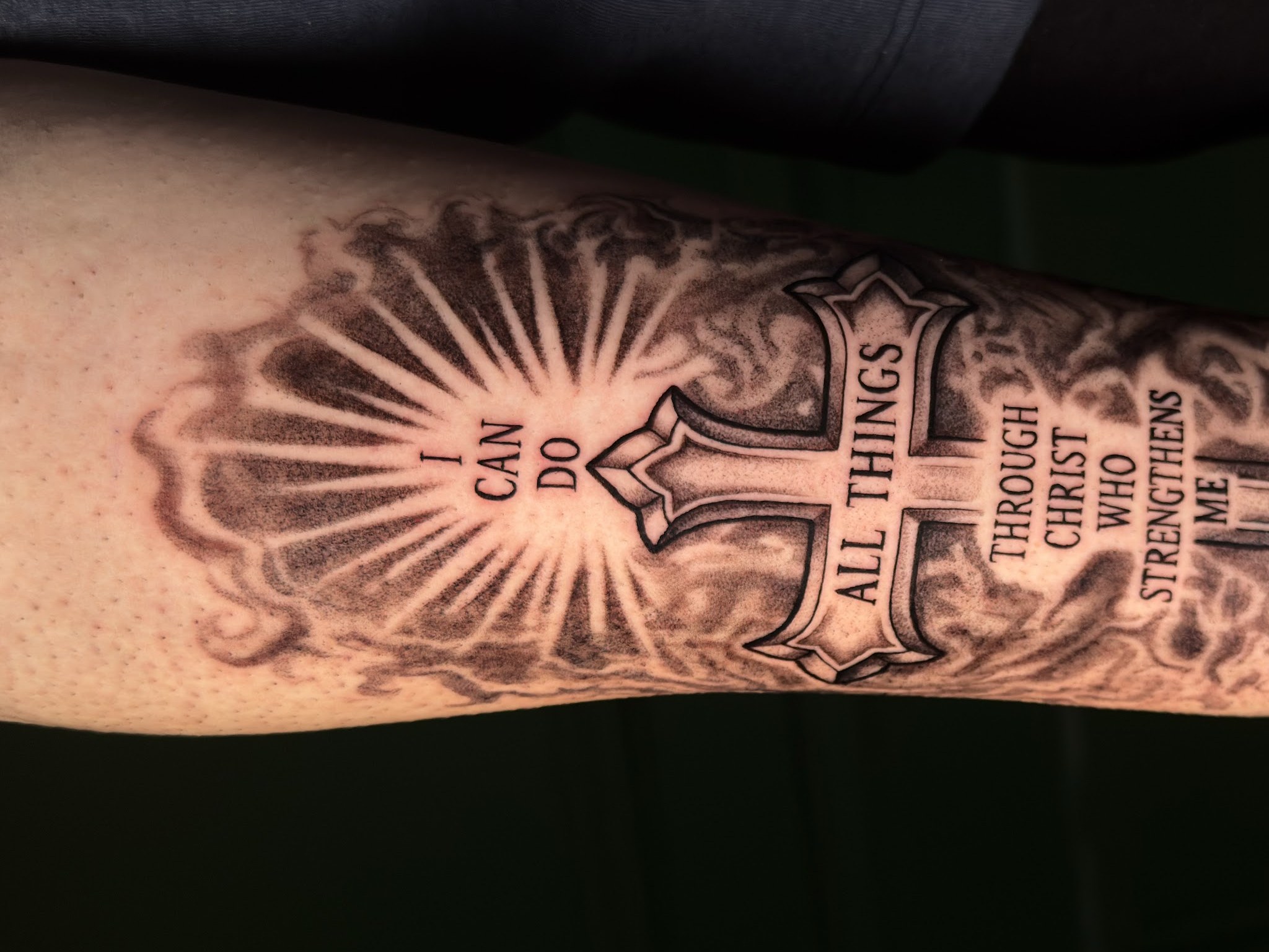 Lettering op een onderarm: I can do all things through Christ who strengthens me, met een kruis en stralen