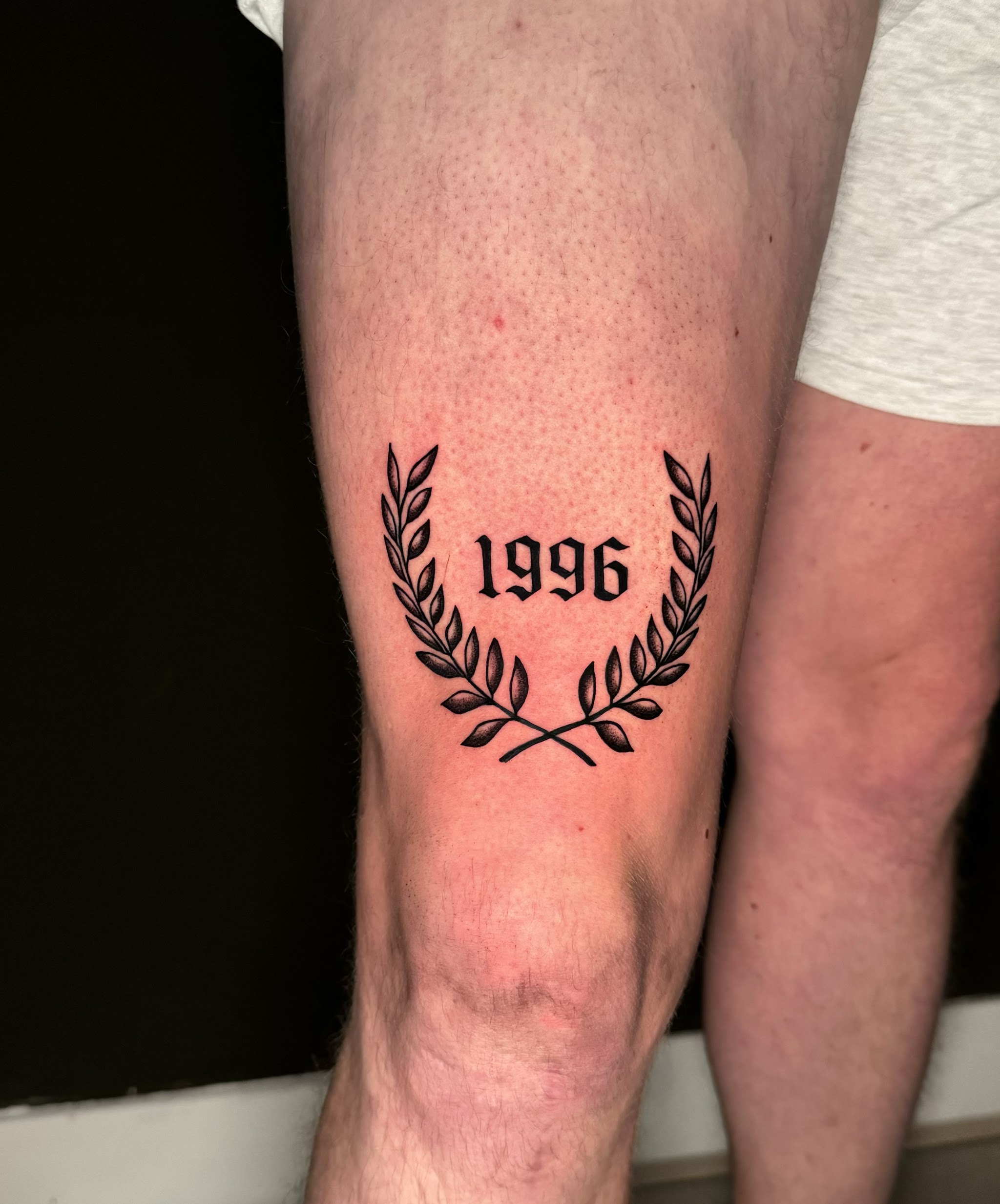 Het jaartal 1996 in blackletter, in een lauwerkrans, op een bovenbeen