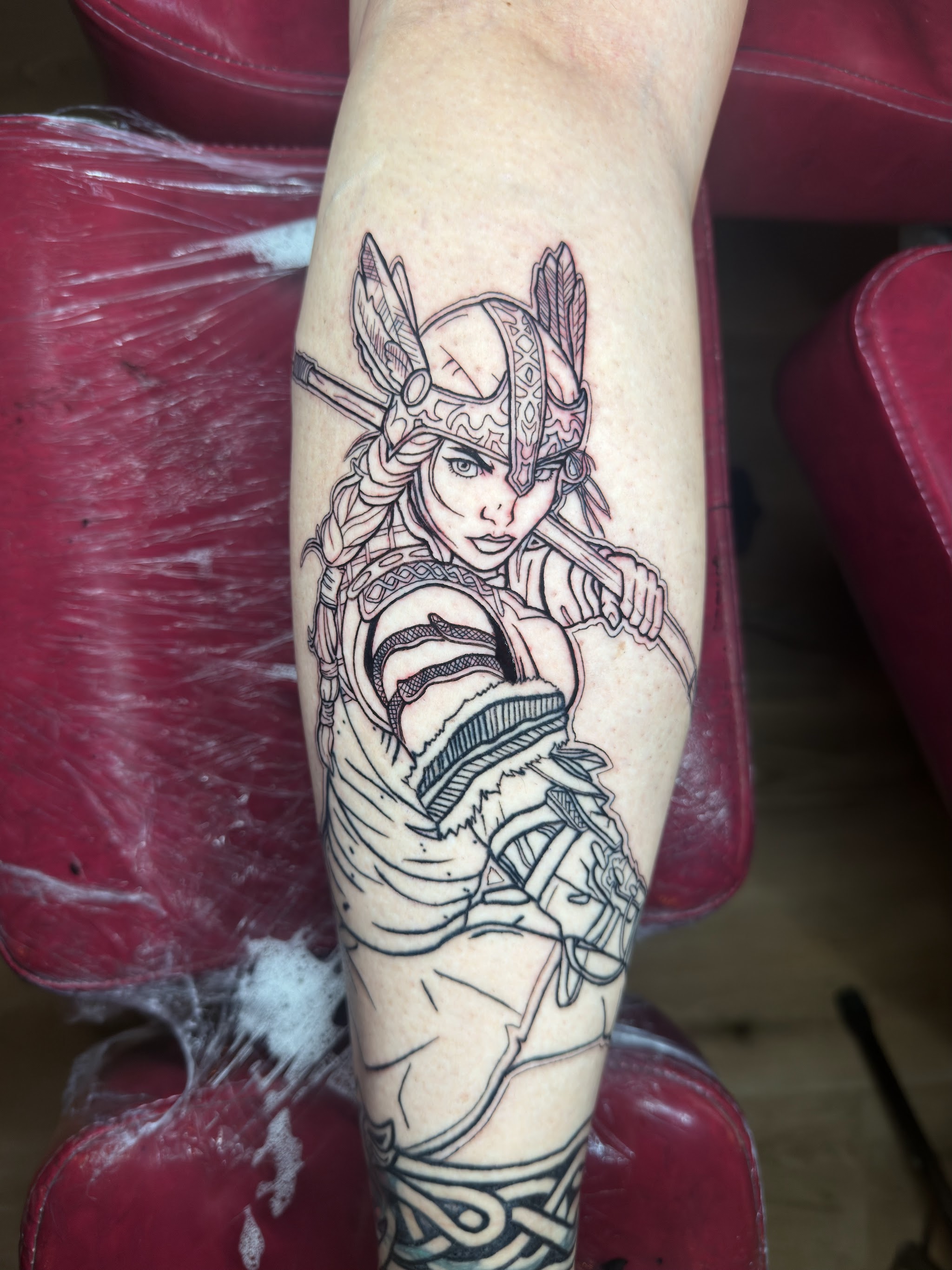 Lijnwerk van een valkyrie op een kuit, halverwege de sessie, in de rode tattoostoel